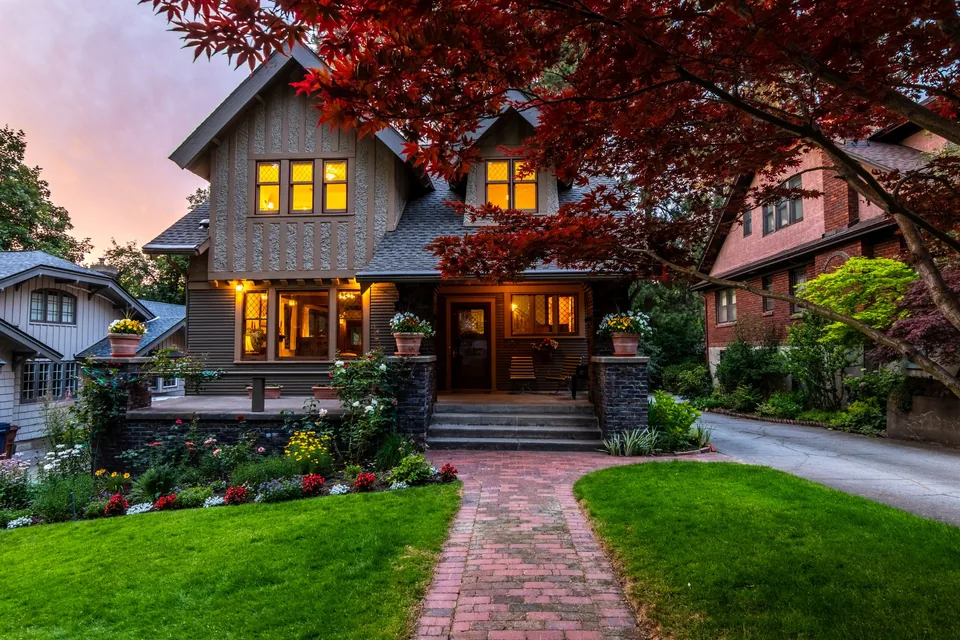 A home wrapped in a lush garden at twilight, every window lit gold