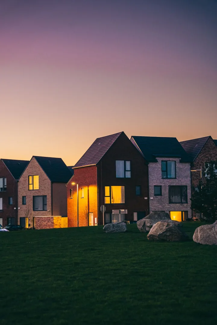 New brick homes at twilight under a peach-to-lavender sky, windows glowing warm