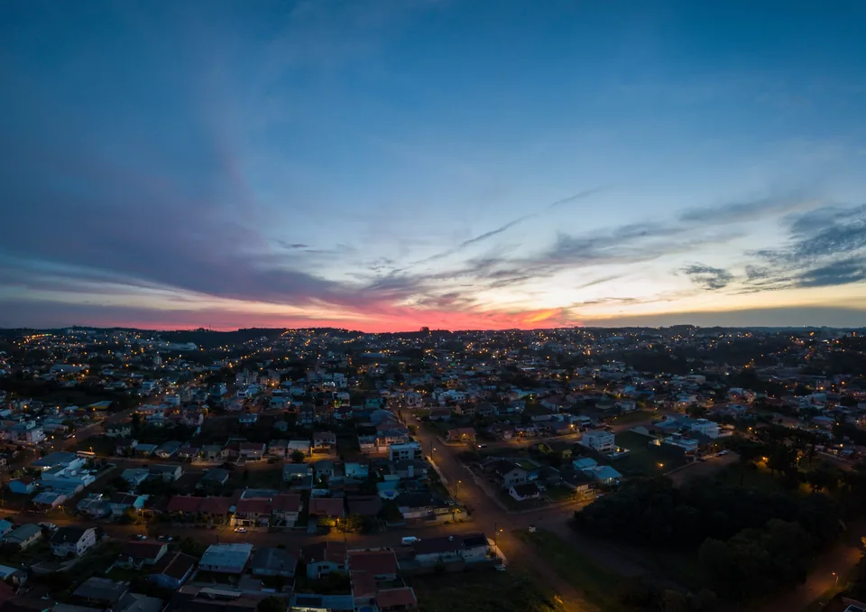 A suburb at sunrise under a band of pink cloud, a few lights on