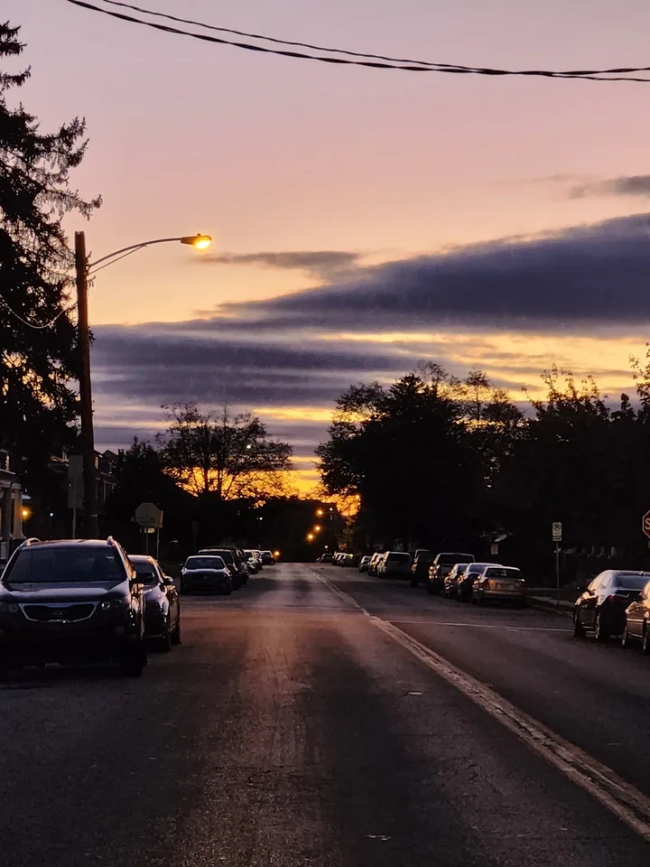 A quiet suburban street at sunset with one streetlight on