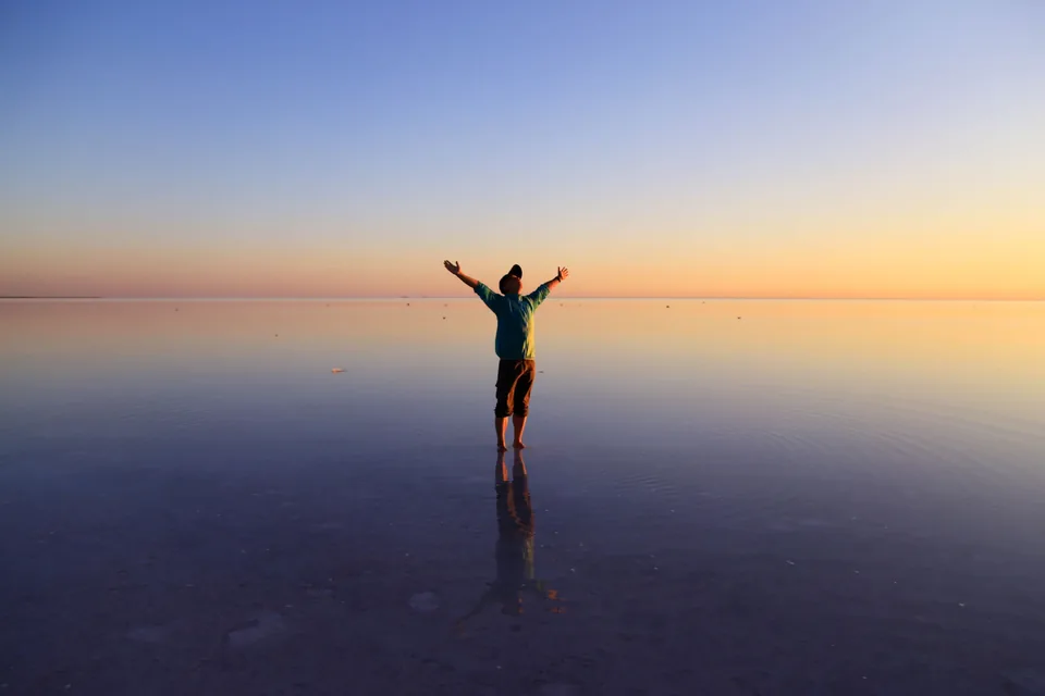 A person standing with arms open on mirror-still water at sunset