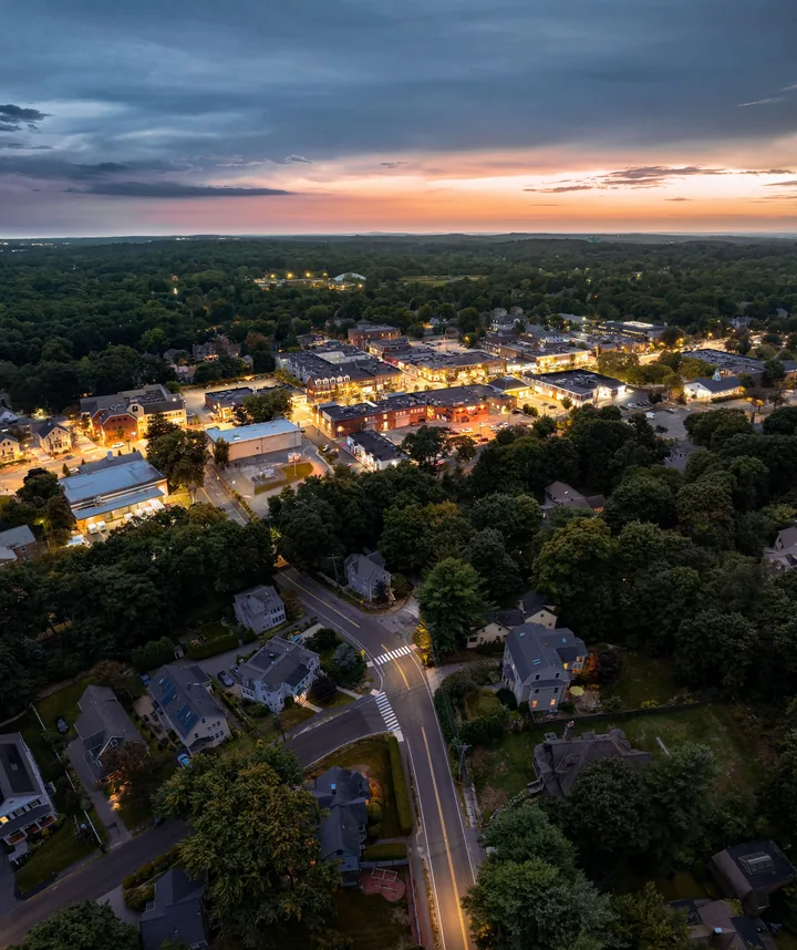 A lush town at dusk from the air, streetlights coming on