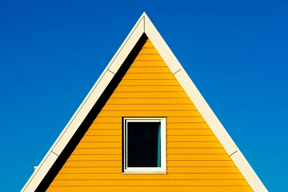 A sunny yellow timber gable with one centred window against a clean blue sky