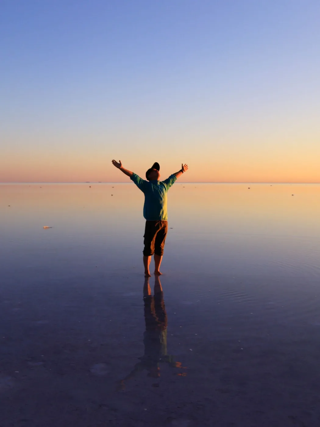 A person standing with arms open on mirror-still water at sunset